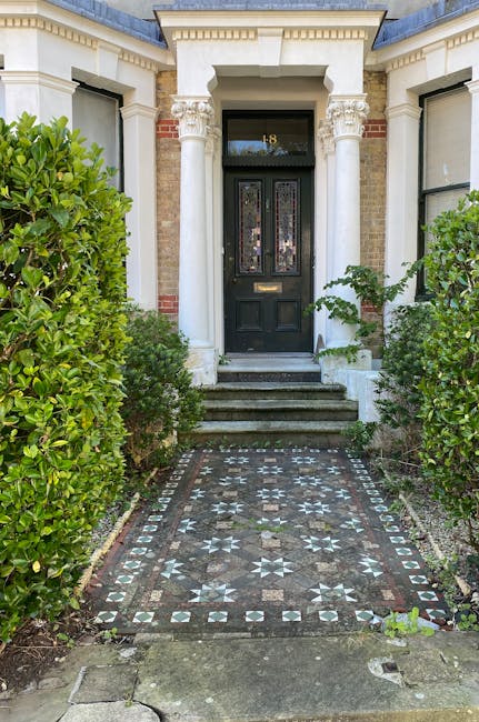 A view of a staircase leading down to a tiled hallway in a historic building, featuring a decorative rounded archway with intricate molding framing the entrance. The staircase has a striped carpet run
